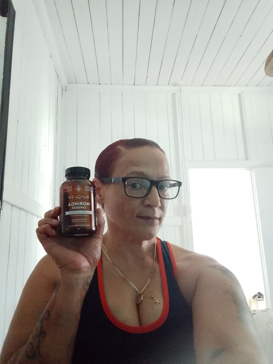 Woman holding a bottle of Forest Super Foods Moringa capsules, sharing her experience with moringa benefits such as energy support, anti-inflammatory properties, and healthier skin and hair.